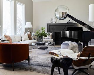 Bright, modern living room with black piano, black marble fireplace, round mirror, white leather vitra eames armchair, gray rug, sofa, glass coffee table