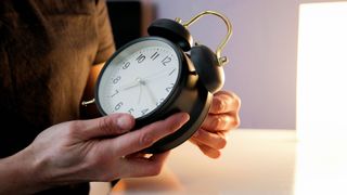 photo of a woman&#039;s hands holding a large table-top alarm clock and adjusting the time