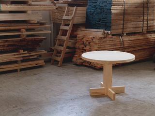 Round dining table in pine wood photographed near stacks of wood