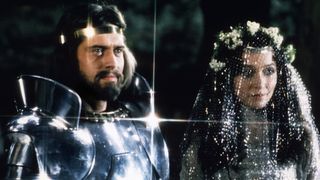 King Arthur stands in armor beside Guenevere in Exclaibur