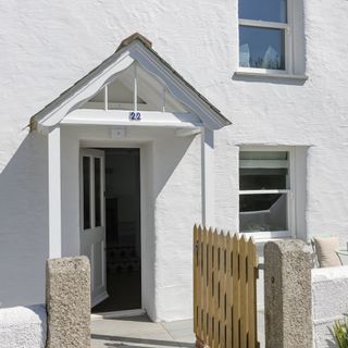 Outside of a white cottage with a wooden gate and an open door