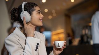 Sony WH-1000XM5 in white being used by a woman drinking a coffee
