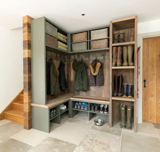 boots and coats stored in mudroom with painted wooden shelves with exposed wooden trim and natural wood staircase