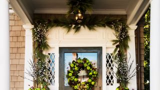 Front door with Christmas decorations featuring apples on a wreath with a garland used above the door as an extra Christmas decorating idea