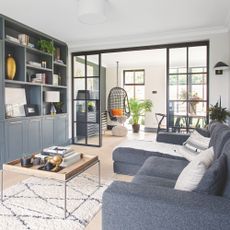 Open plan living area with blue sofa and blue media wall, leading into the dining room
