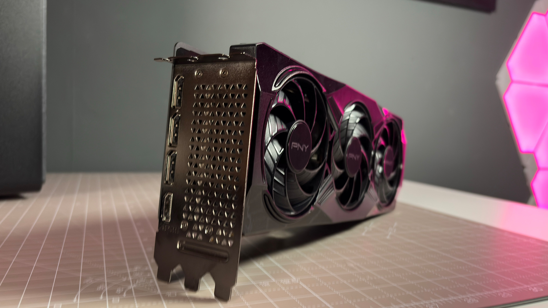 A PNY RTX 5070 Ti OC graphics card on a desk with a desk mat and pink light.