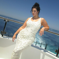 Photo of Ashley Graham wearing white floral embroidered maxi dress while standing on yacht.
