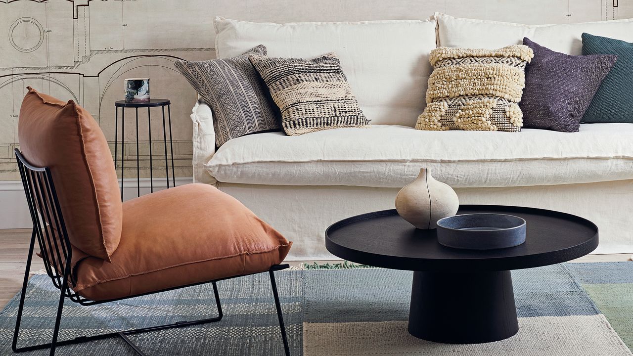 A white sofa in a living room with a black accent chair with burnt orange cushions and a circular black coffee table