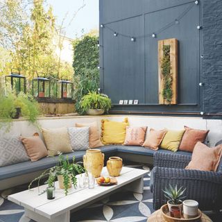 Outdoor seating area with concrete bench covered in cushions and lighting on the wall above