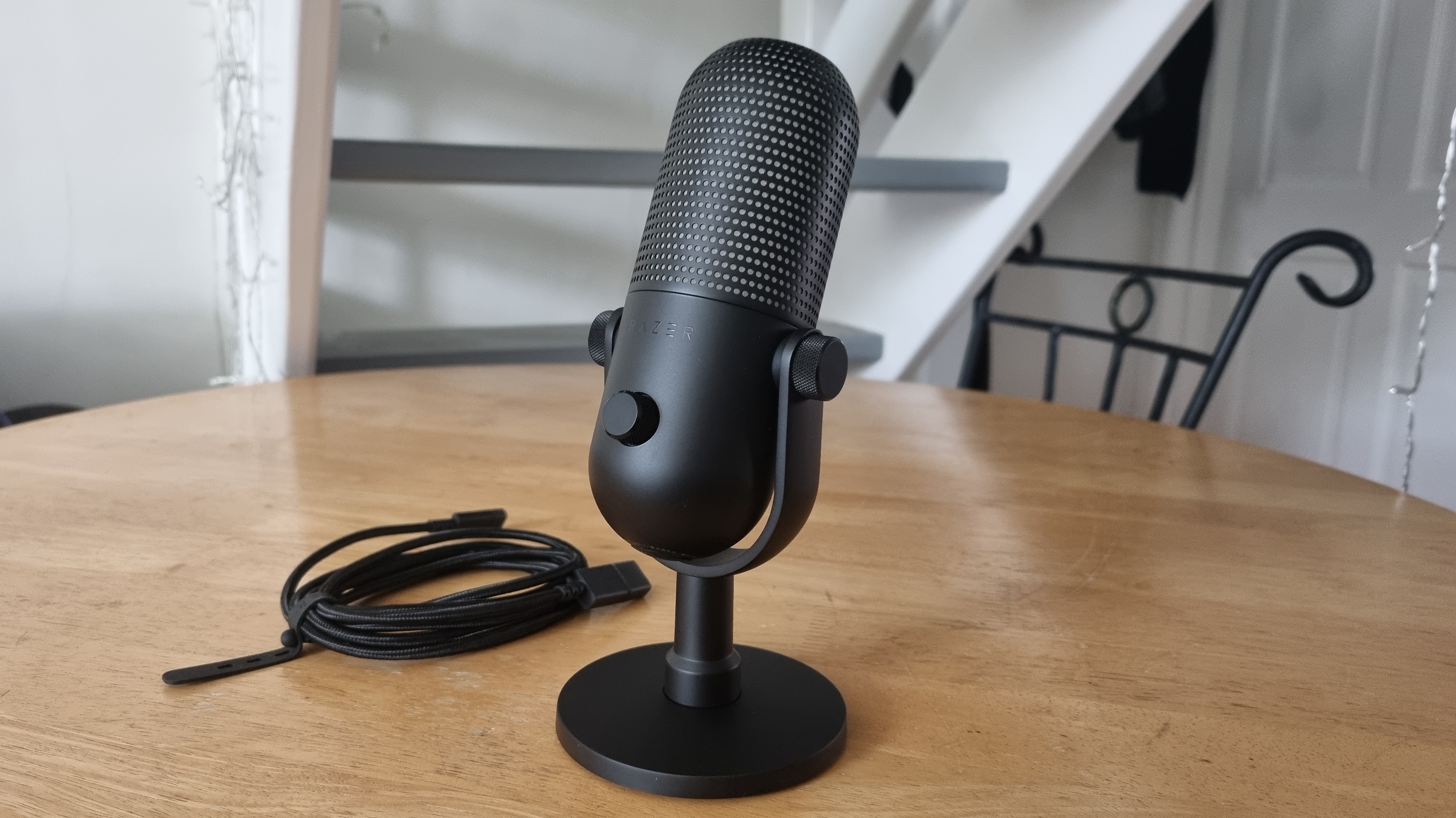 The Razer Seiren V3 Chroma microphone on a desktop, lights off, with the included cable