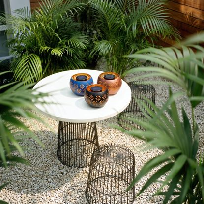Aldi's Belavi solar light fire bowls on a small table in a modern garden with foliage all around