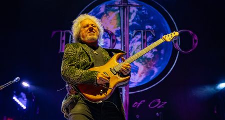 Steve Lukather solos on his natural finish Ernie Ball Music Man Luke signature guitar at a recent Toto show &ndash; the band's logo is emblazoned across Planet Earth in the background.