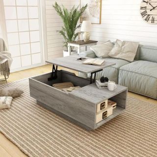 Grey lift top coffee table with side shelving built-in sitting in living room on striped rug with grey sectional sofa beside it