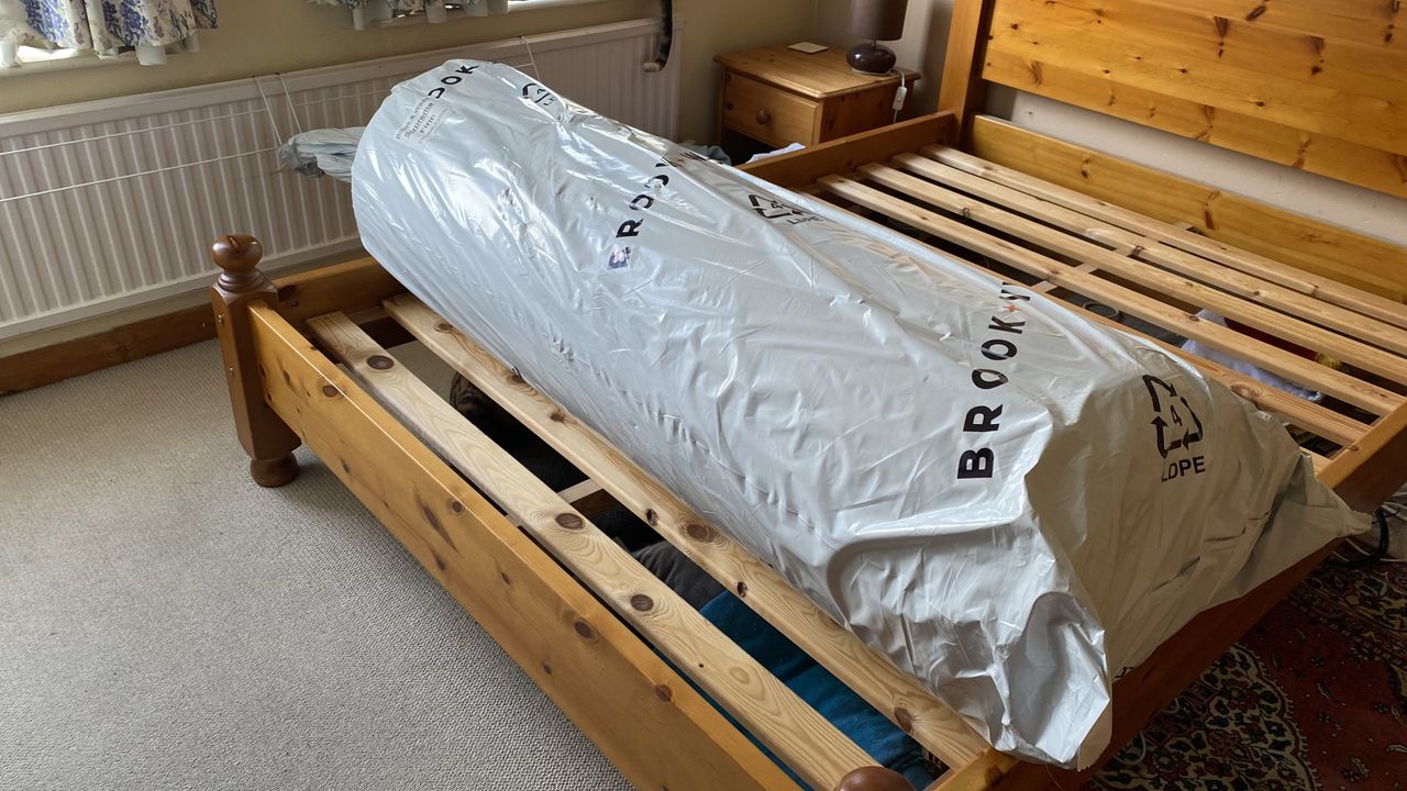 Brook + Wilde Suprema Mattress review image shows the matress rolled up in packaging on our tester's wooden bed frame