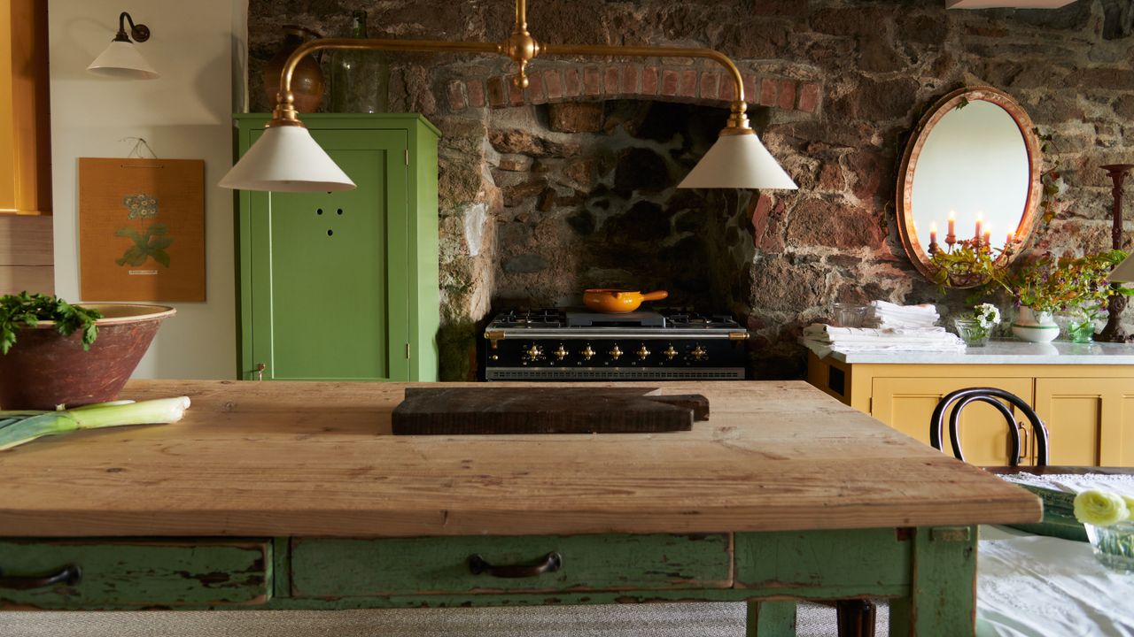 green and yellow farmhouse style kitchen with freestanding furniture, enamel lights, stove, original bricks, napkins/tablecloth, mirror