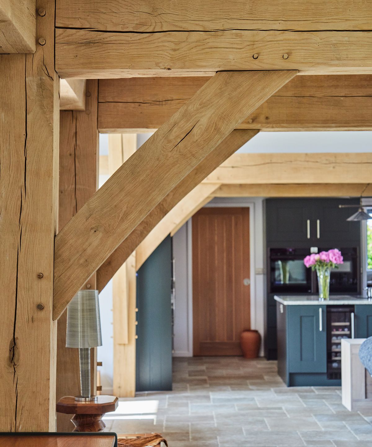 Exposed beams in an oak-frame self-build with a kitchen in the background and stone floor