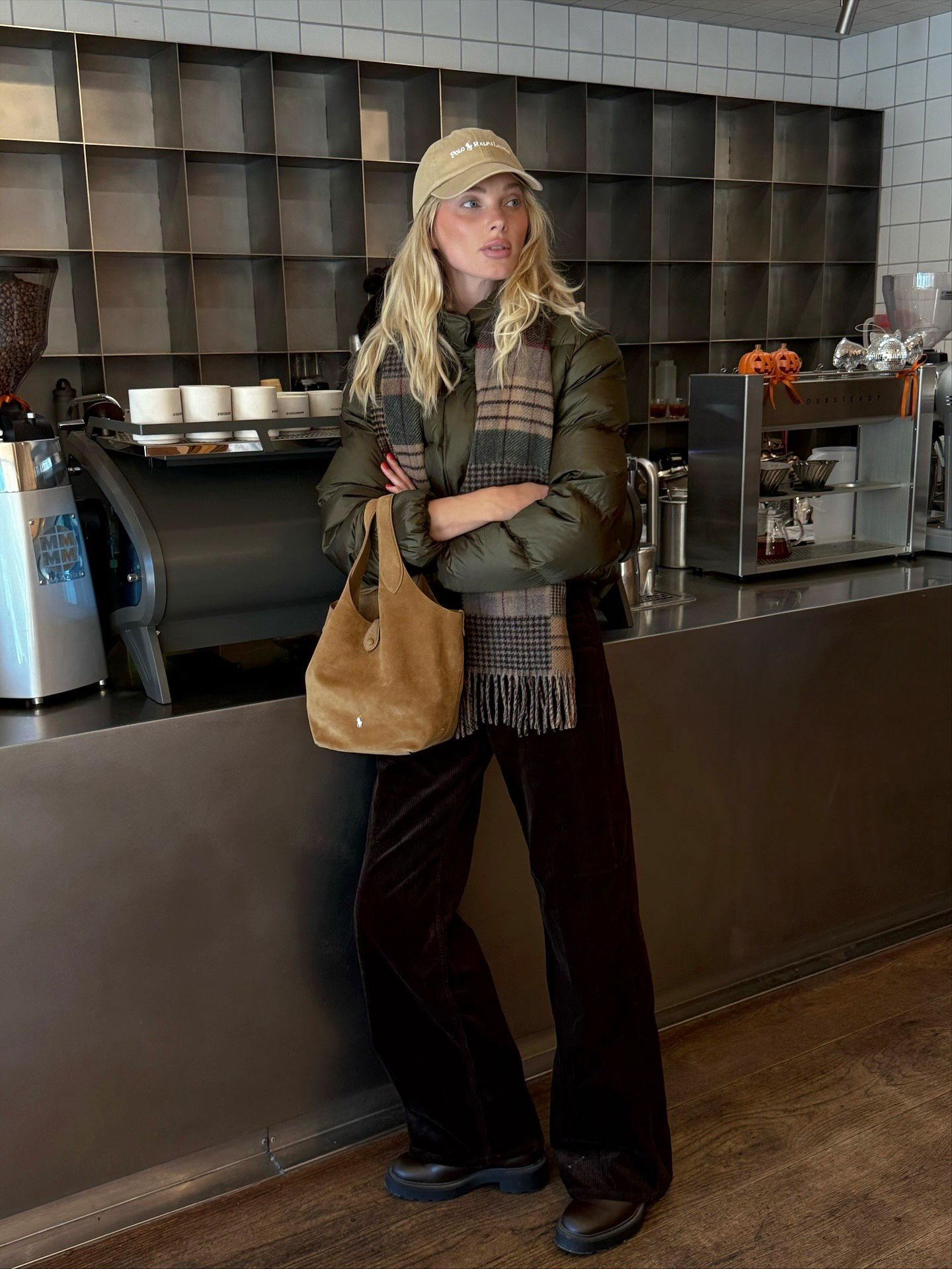 Elsa Hosk wearing a Polo Ralph Lauren baseball cap, olive green puffer jacket, plaid scarf, black pants, and boots