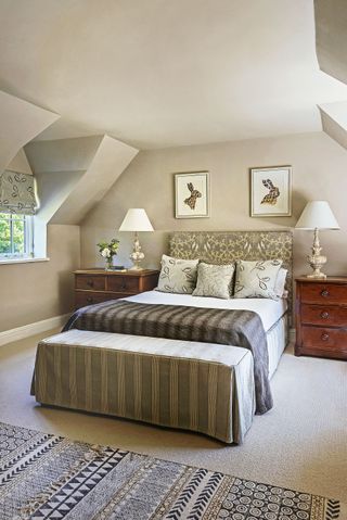 double bedroom with dormer windows and neutral color palette with bench at foot of bed