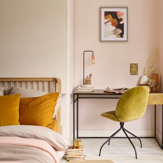 small bedroom colour ideas, bedroom with off white and pale blush walls, bed with saffron pillows, pale pink bedding, white painted floor, desk for working, artwork, lime velvet desk chair, desk lamp, books