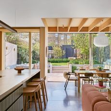 an open plan kitchen, dining and living area with slatted roof panels, a dusky pink sofa and a large kitchen island