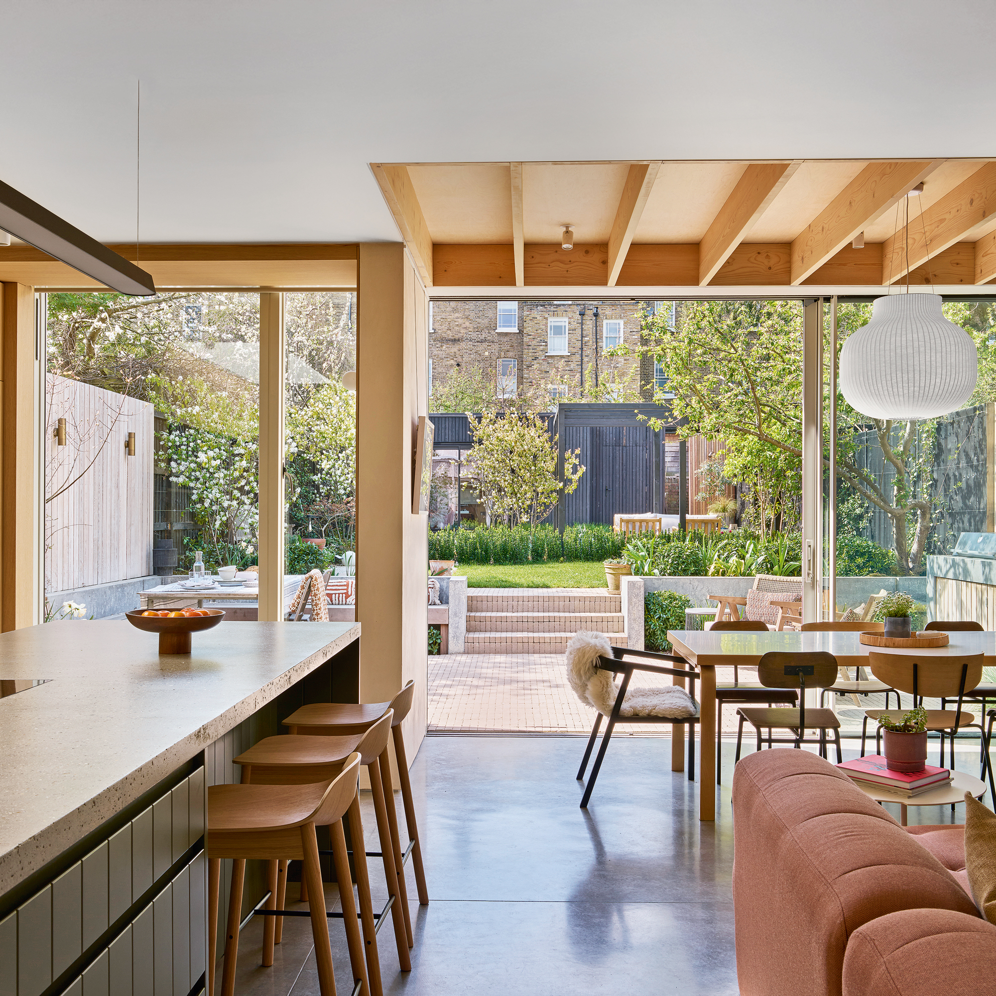 an open plan kitchen, dining and living area with slatted roof panels, a dusky pink sofa and a large kitchen island
