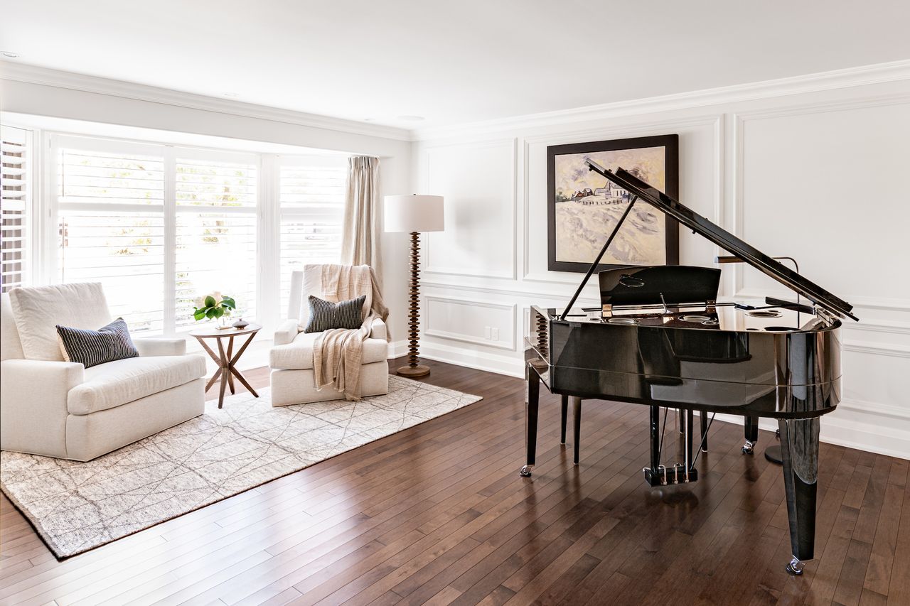 A music room with a large black grand piano and two white armchairs 