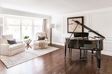 A music room with a large black grande piano and two white armchairs 