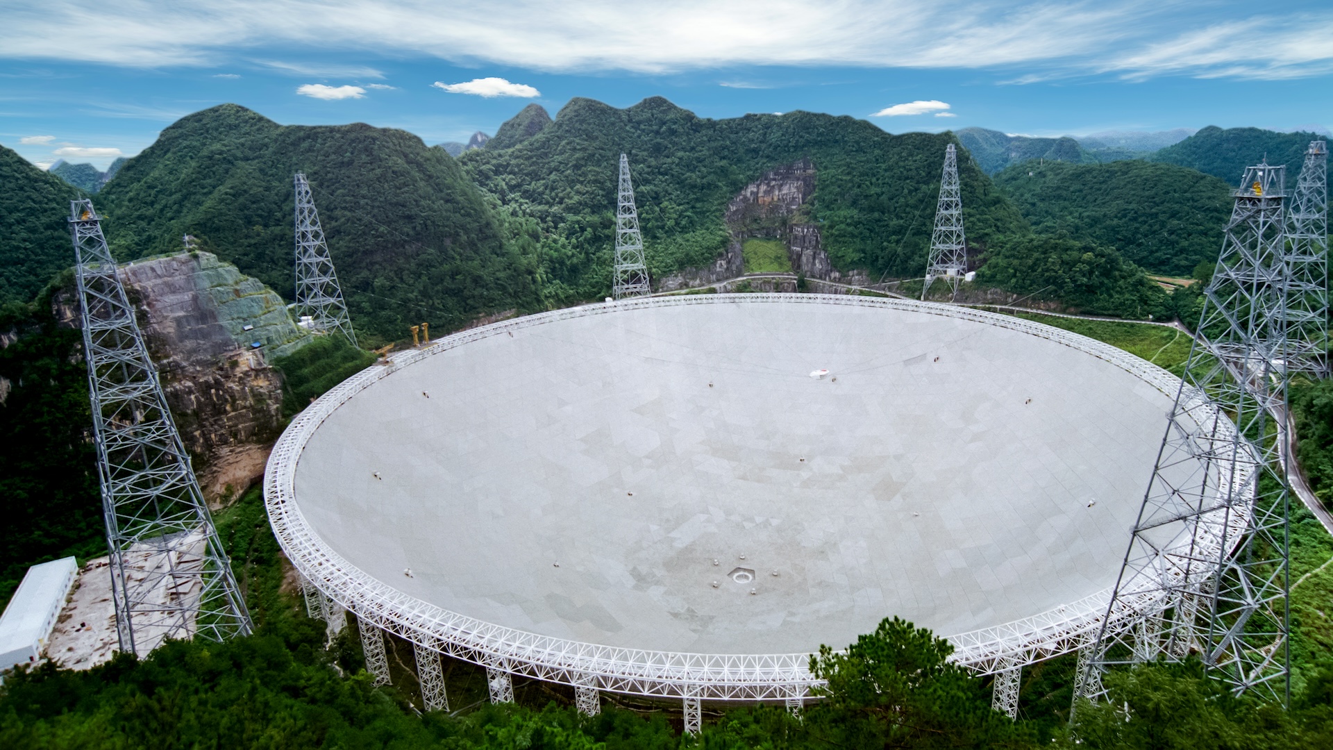 An aerial image of a massive telescope and related equipment in the middle of rolling green hills