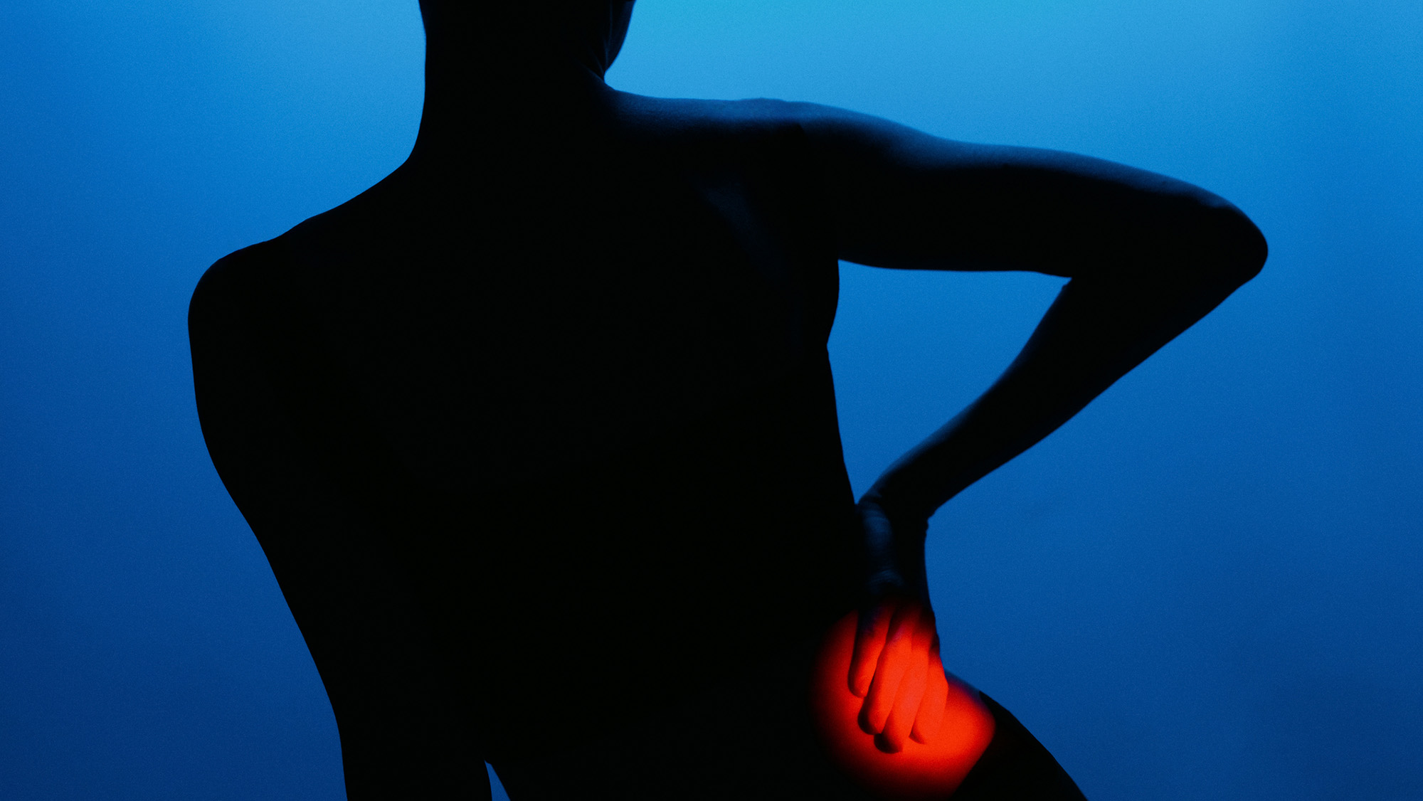 A silhouette of a person holding their side with a red light where their hand is touching their lower side.