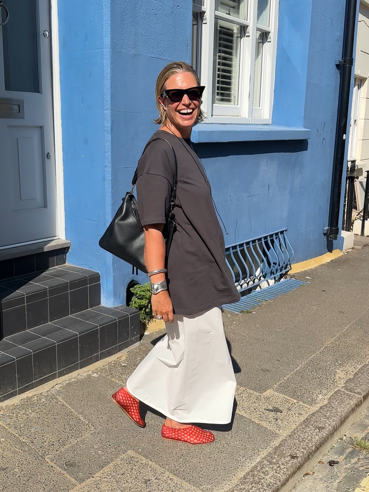dated summer shoe trends 2026: alexis foreman wears a grey t-shirt, white maxi skirt and red jelly ballet pumps