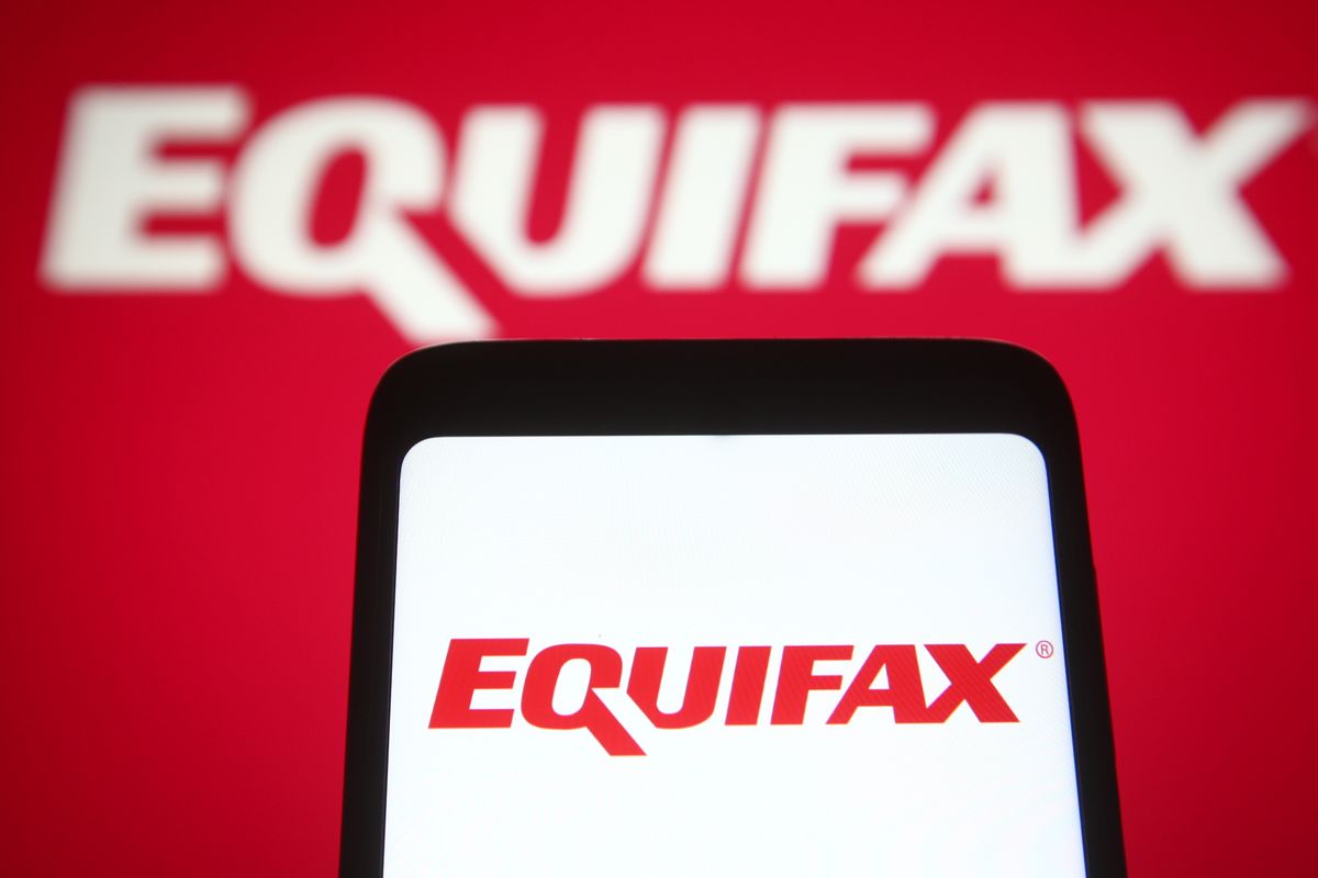 Equifax logo held up on a smartphone screen with logo in background