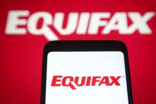 Equifax logo held up on a smartphone screen with logo in background