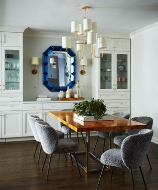 Jewel thick trim angular mirror at the head of a dining room table reflecting artistic pendant lighting