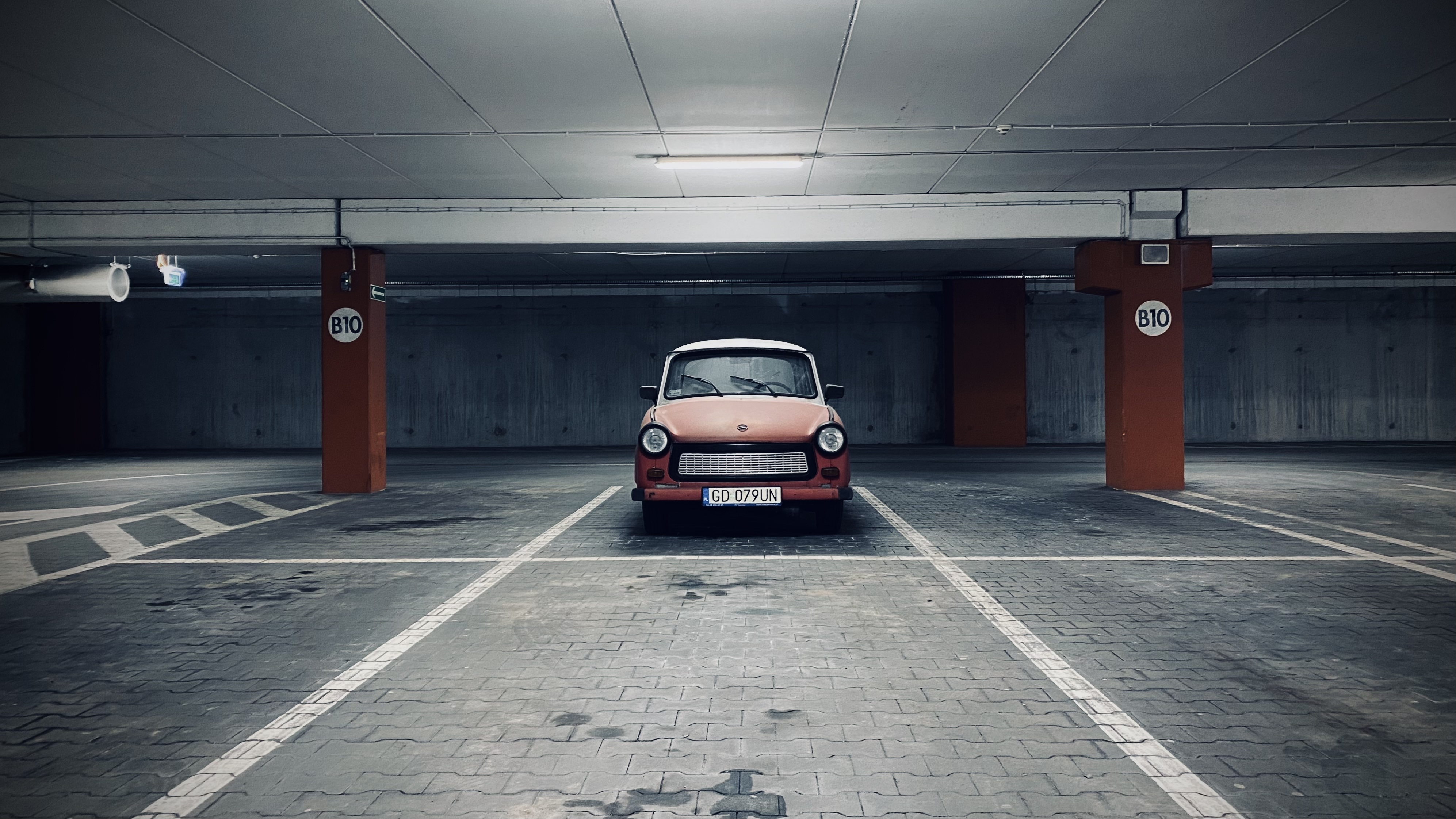 An old car under a spotlight in an empty underground parking lot