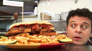 Adam Richman with his head on a table next to The Ultimate Destroyer challenge