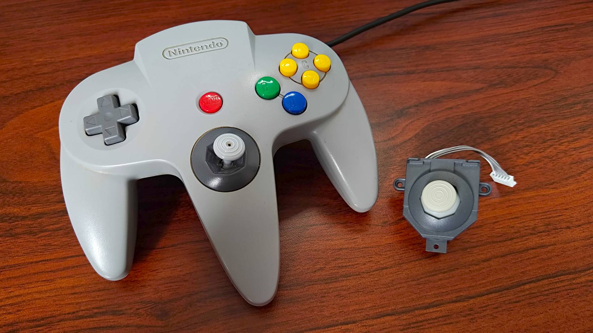 N64 controller next to Hyperkin hall-effect joystick on woodgrain desk.