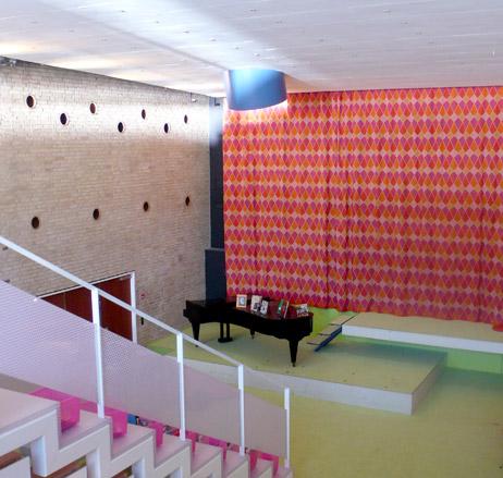 A bright white staircase leading down to a grand piano with brightly coloured curtains behind.