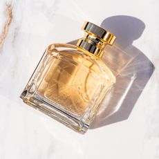 Bird's eye view of a perfume bottle filled with gold perfume laying on its side against a white and bronze marble counter