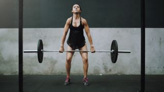 Woman performs clean and press, she is midway through the clean movement moving the bar past her thighs