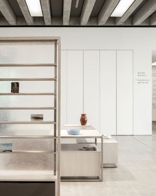 Close up view of a shelving unit with a frosted back and three items on display at the Turner Contemporary shop. Behind the shelving unit are white and grey tables with items on top in a space with white walls and light grey flooring