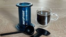 AeroPress Clear Color coffee press in blue with accessories and coffee mug
