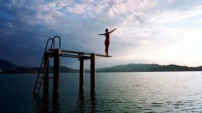 A woman stands poised on the end of a diving board.