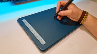 A photo of the blue XP-Pen Deco MW tablet on a white desk being used with the stylus.