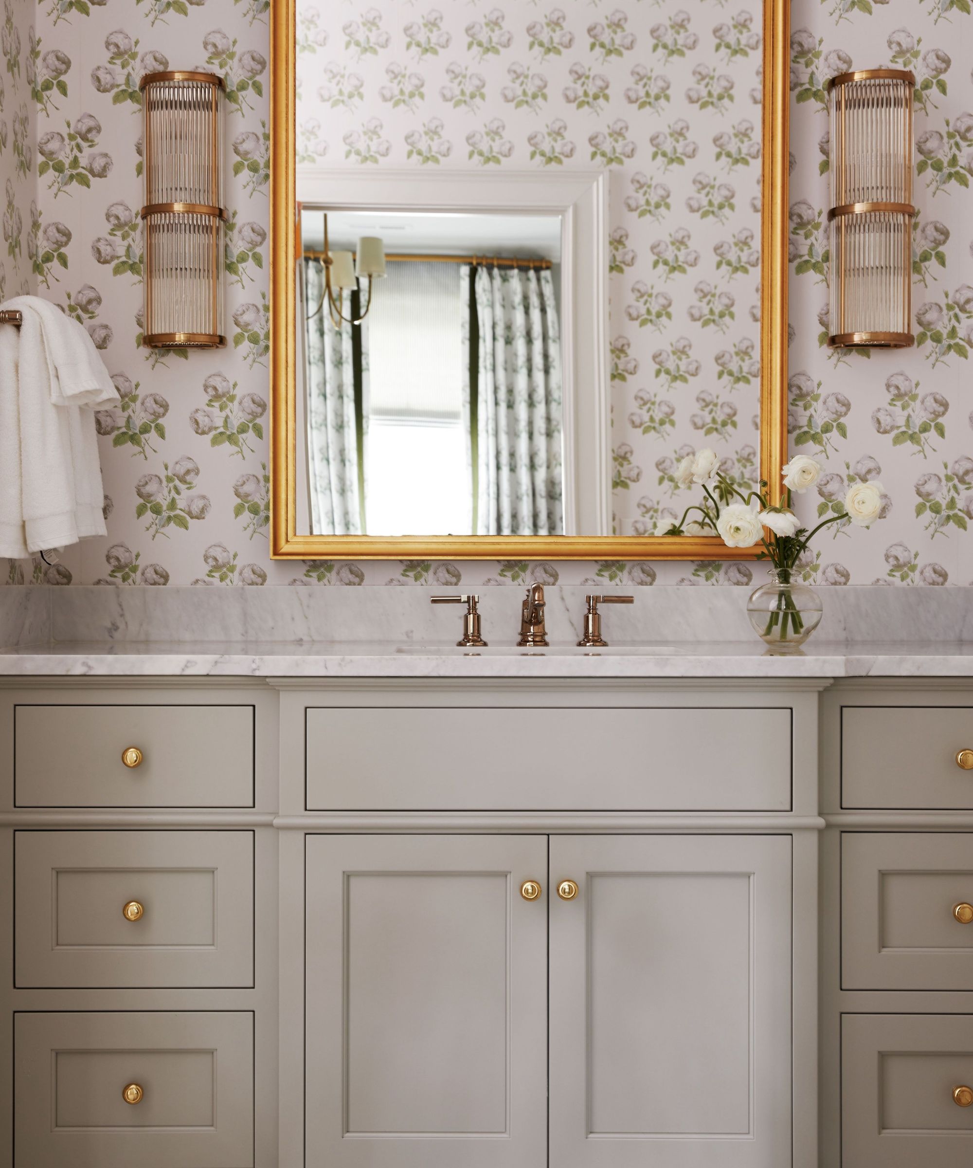 A bathroom with neutral floral wallpaper, a greige vanity and a wall mirror.