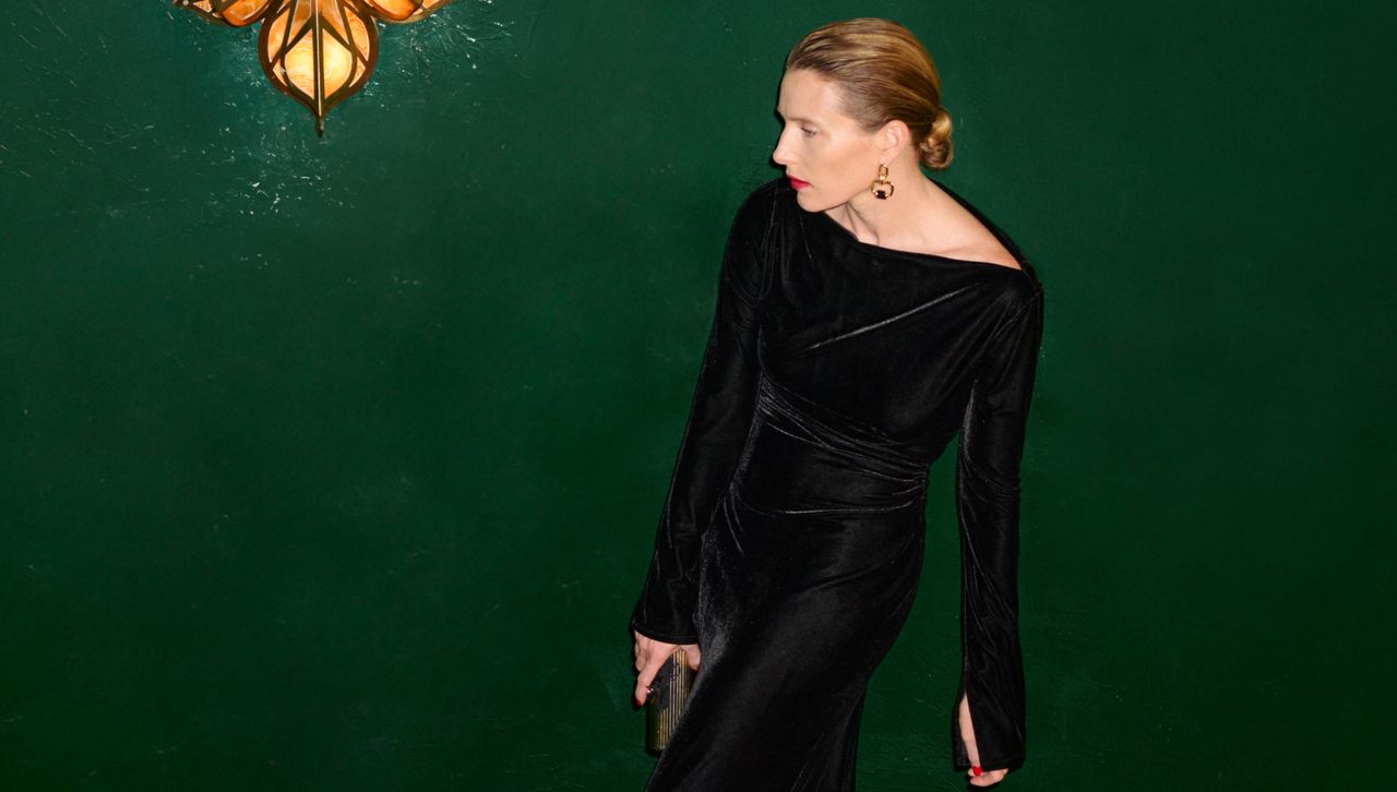 a model wears a velvet dress with a low bun and earrings designed by clare waight keller in front of a green wall