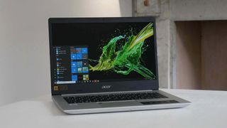 Bästa billiga laptop: En Acer Aspire 5 står öppnad på ett vitt bord med en svart och grön bakgrundsbild som visas på skärmen.