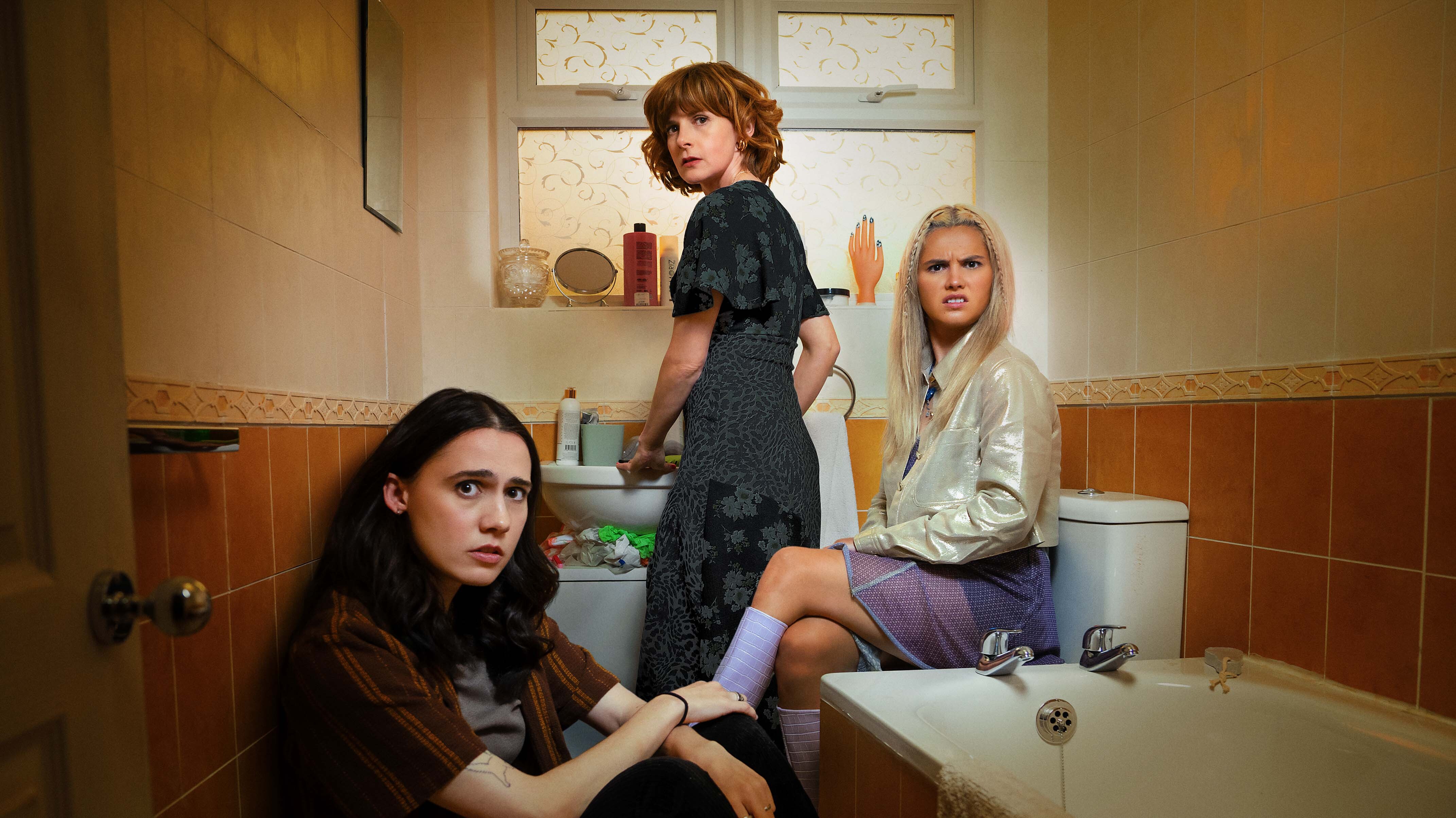 Josie sitting on the floor of the bathroom with mum Deb at the sink and sister Billie on the toilet.