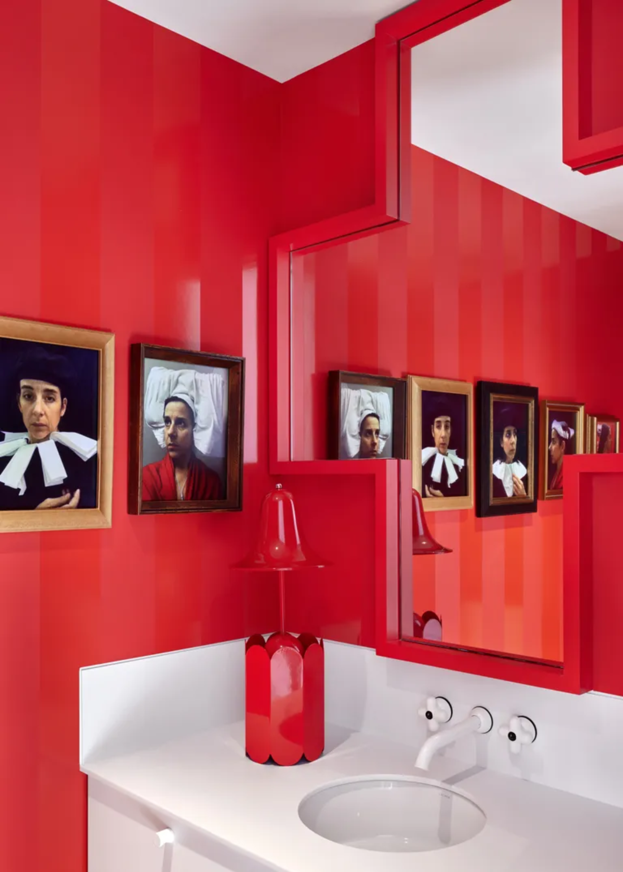 A ruby red bathroom with framed art, a bright table lamp and a white basin