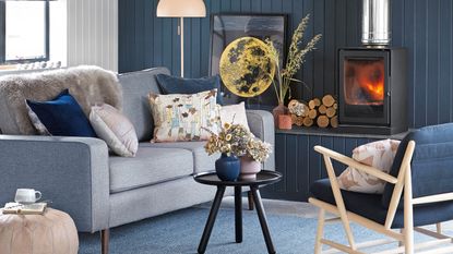 Armchair and coffee table pulled up in front of a marble fireplace with fire burning and lots of natural materials on display