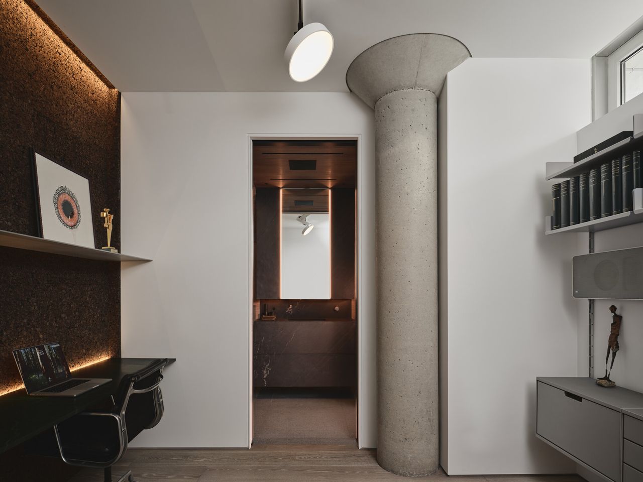 home office with concrete pillar, shelving, desk with cork wall and floating shelves looking through to a bathroom